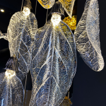 Close-up of sculpted optical acrylic leaf blade showing realistic leaf vein textures and flower-bud cap light source on a luxury chandelier