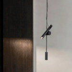 Architectural black iron and aluminum spotlight pendant projecting warm directional light onto a textured dark wood wall