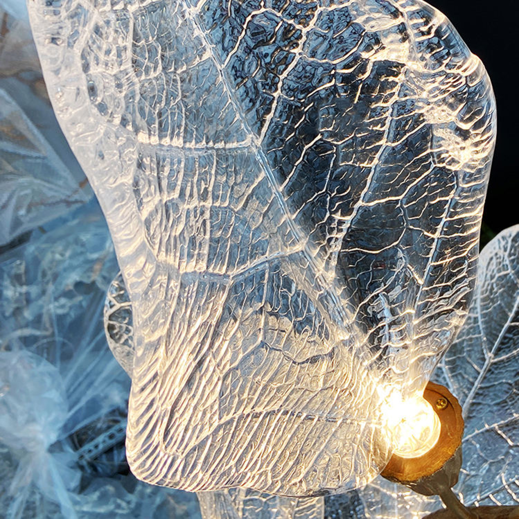 Close-up of sculpted optical acrylic leaf blade showing realistic leaf vein textures and flower-bud cap light source on a luxury chandelier
