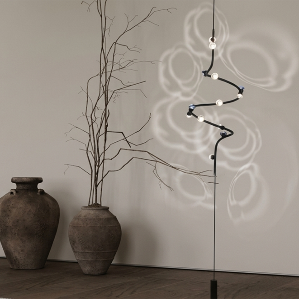 Floor-to-ceiling spiral chandelier with black iron and aluminum frame projecting floral ripple light shadows through crystal lenses onto a neutral wall