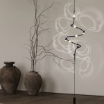 Floor-to-ceiling spiral chandelier with black iron and aluminum frame projecting floral ripple light shadows through crystal lenses onto a neutral wall