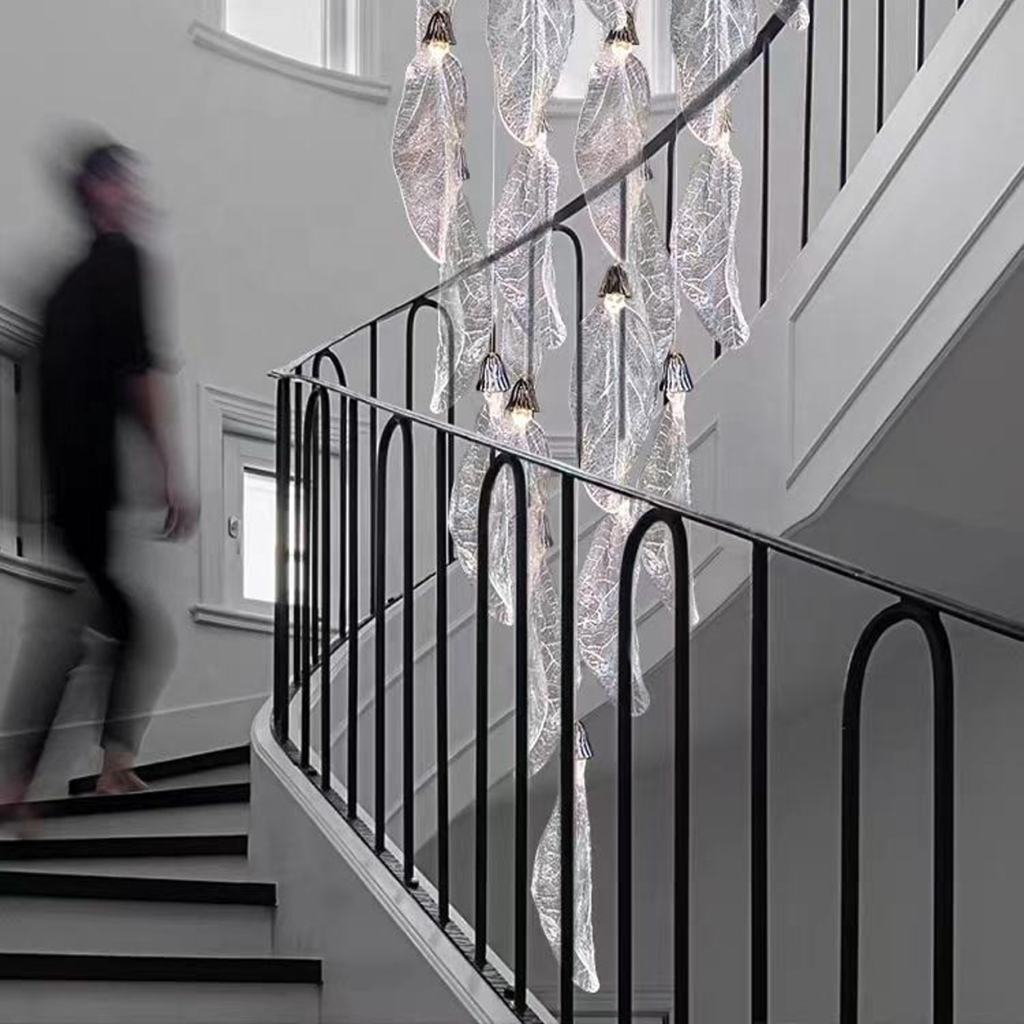 Tall stainless steel and textured acrylic leaf cascade chandelier suspended in a high-ceiling stairwell void