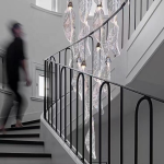 Tall stainless steel and textured acrylic leaf cascade chandelier suspended in a high-ceiling stairwell void