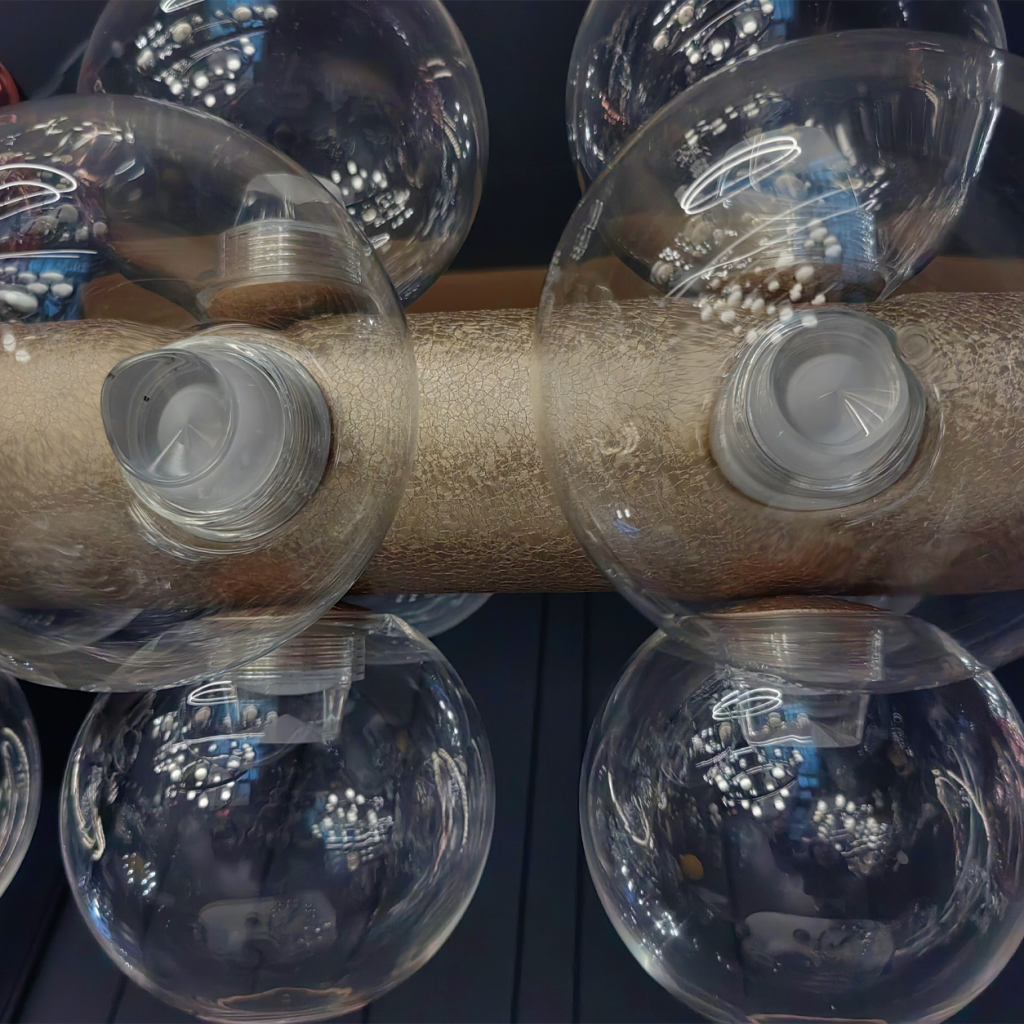 Close up of clear glass globe threaded sockets on textured gold linear pendant light body