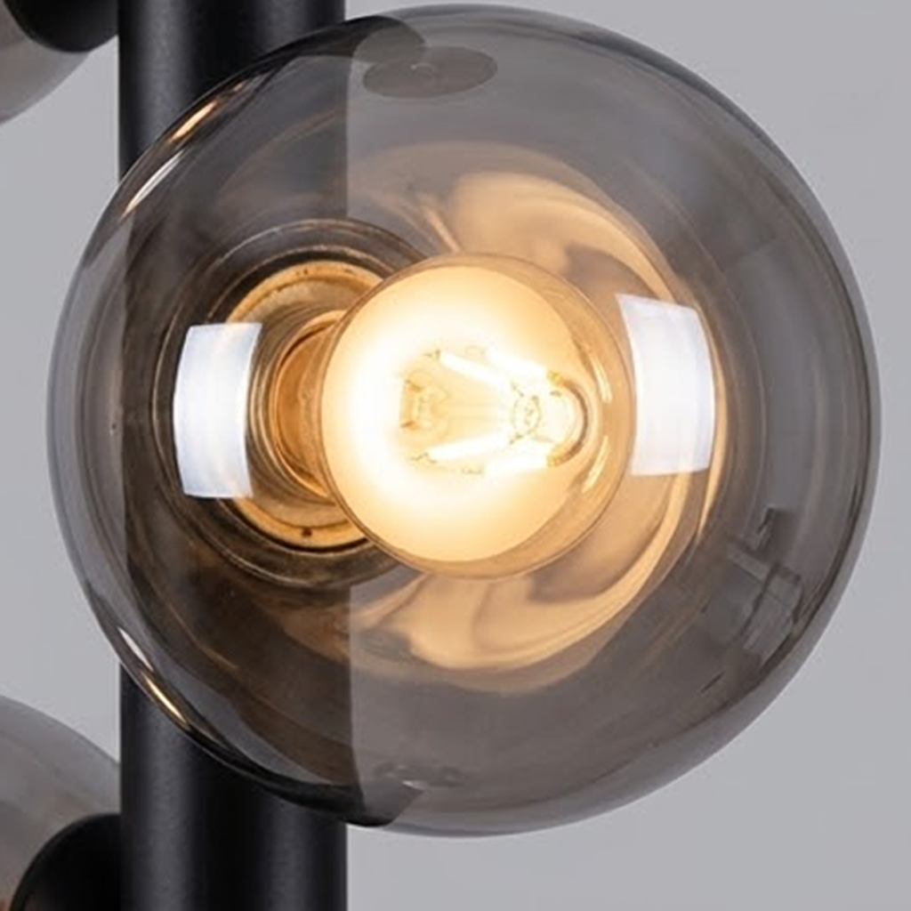 Close up of smoky glass globe shade with warm exposed LED filament bulb on matte black stem