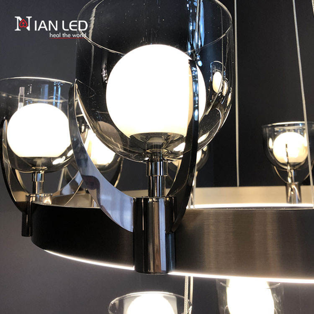 Close-up of clear glass cup shade with inner glowing bulb held by mirror brown stainless steel bracket on brushed brown ring frame