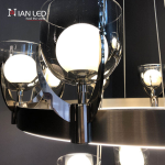 Close-up of clear glass cup shade with inner glowing bulb held by mirror brown stainless steel bracket on brushed brown ring frame