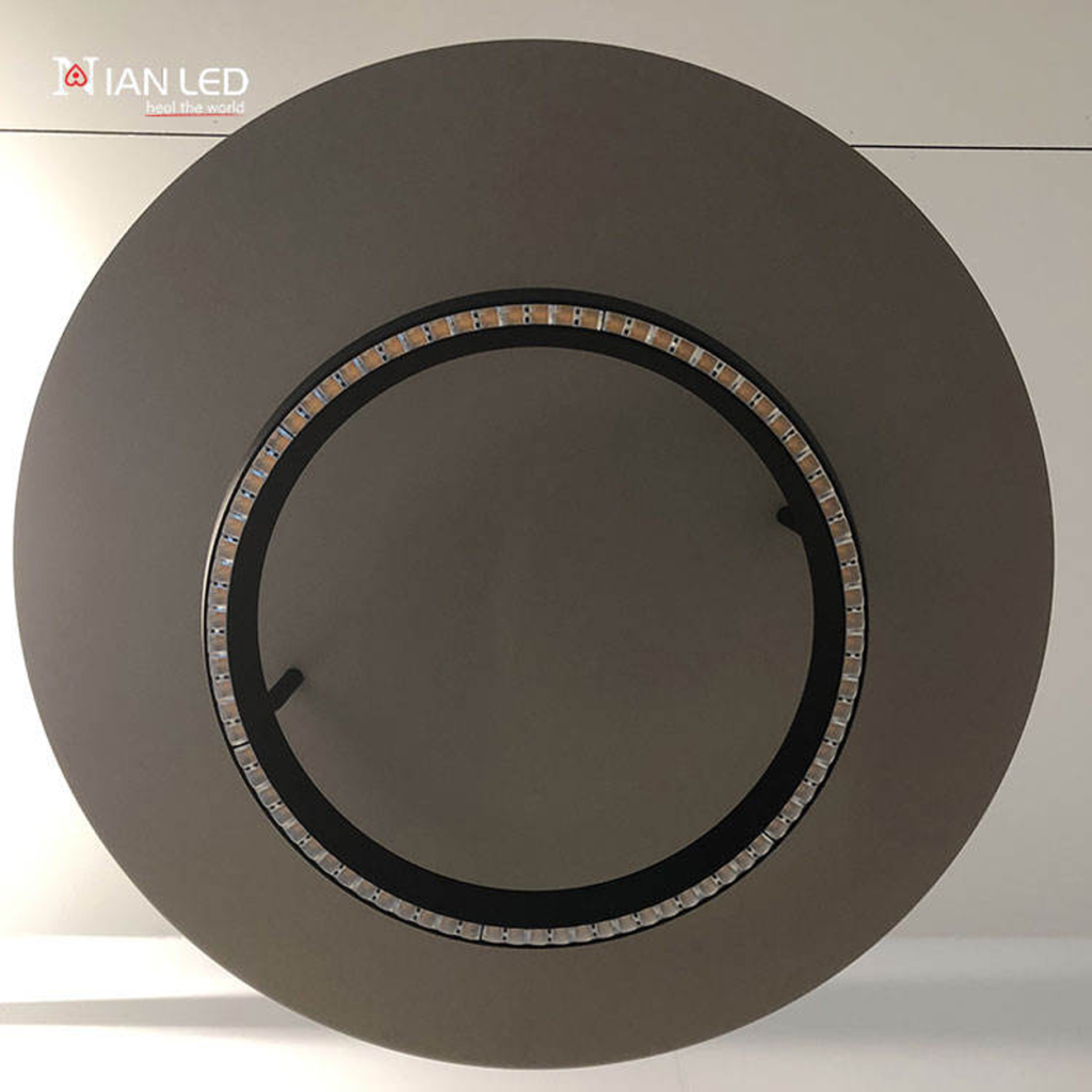 Upward view of glowing black aluminum LED ring showing micro-lenses and illuminated warm aluminum reflector disc