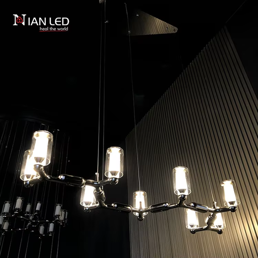 Glowing modern branching node linear LED chandelier with glass cylinder cups illuminated against dark textured wall