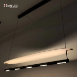 Modern surfboard linear aluminum pendant light with matte black frame and glowing sandblasted aluminum reflector wing in a dark room